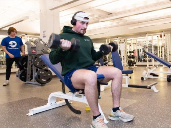 A student lifts weights while seated on a weight bench in one of 91ɫ’s fitness facilities.