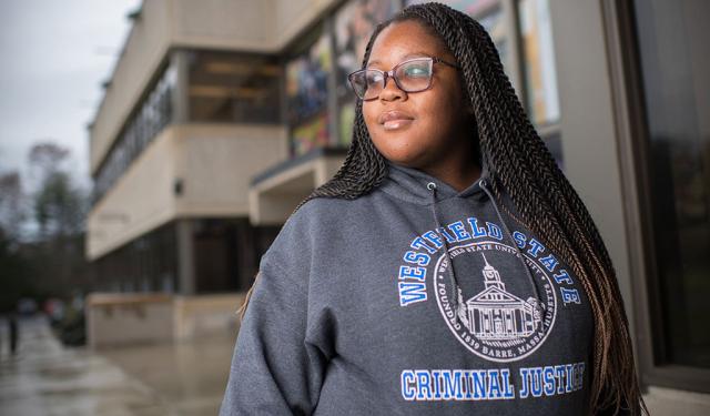 A student poses for a photo while wearing a sweatshirt that says “91ɫ State Criminal Justice.”