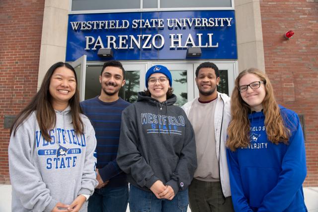 Five students wearing 91ɫ State sweatshirts smiling in front of Parenzo Hall.
