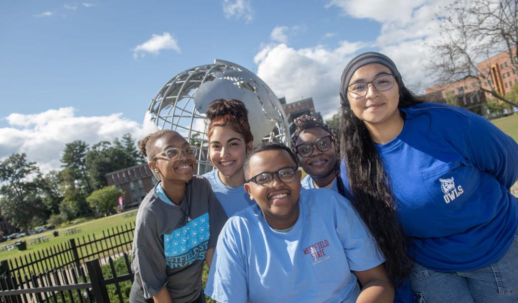 Five students smile while posing for a photo in front of the 91ɫ globe sculpture.