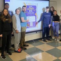91ɫ class of Advanced Public Relations pose in front of a poster design for “Stick Together with Rick’s Place Where Hope Scores Big,” campaign. 