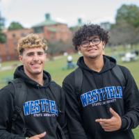 Two students wearing 91ɫ sweatshirts smile while on the campus green.